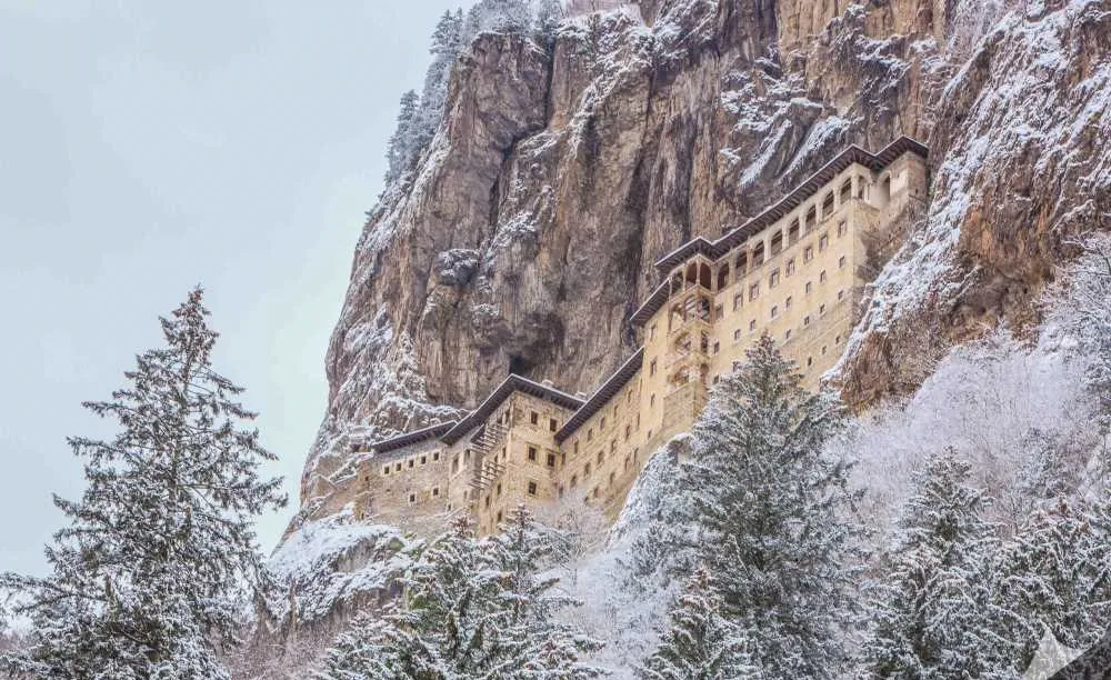 Karla kaplı ağaçlar ve kayalıktaki manastır